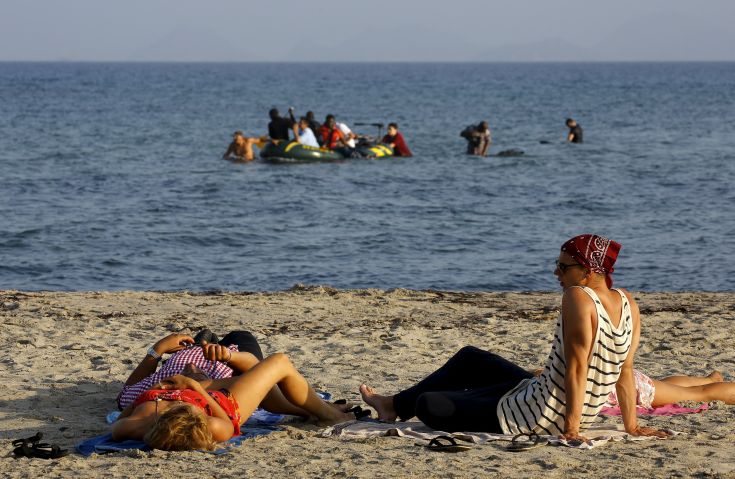Tourists lie on a beach as migrants and refugees from Syria and Africa arrive on a dinghy at the Greek island of Kos after crossing a part of the Aegean Sea between Turkey and Greece, August 8, 2015. The U.N refugee agency, UNHCR, estimates that Greece has received more than 107,000 refugees and migrants this year, more than double its 43,500 intake of 2014. REUTERS/ Yannis Behrakis