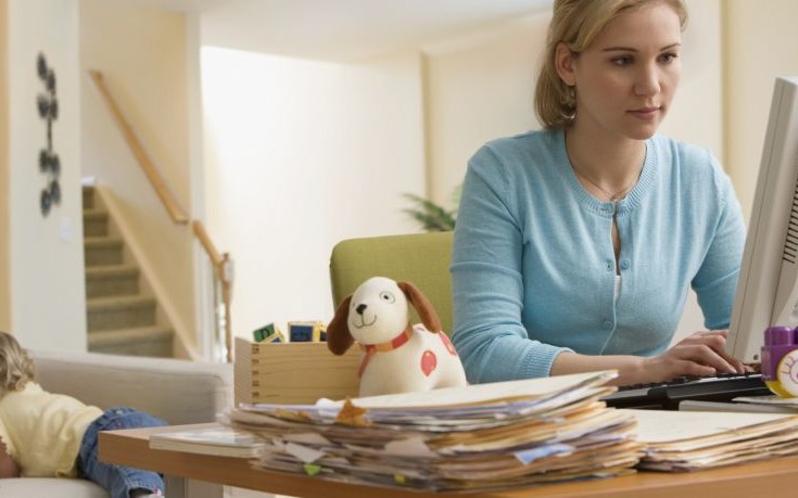 Hispanic woman working at computer with toddler in background