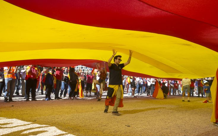 A youth walks under a giant Spanish flag in Madrid, Spain, Saturday, Oct. 7, 2017. Thousands of pro-Spanish unity supporters donning Spanish flags have rallied in a central Madrid plaza to protest the Catalan regional government's drive to separate from Spain. (AP Photo/Paul White)