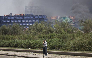 A man adjusts his mask as smoke plumes from the explosion site in Binhai new district in Tianjin, China August 13, 2015. Two huge explosions tore through an industrial area where toxic chemicals and gas were stored in the northeast Chinese port city of Tianjin, killing at least 44 people, including at least a dozen fire fighters, officials and state media said on Thursday. REUTERS/Damir Sagolj