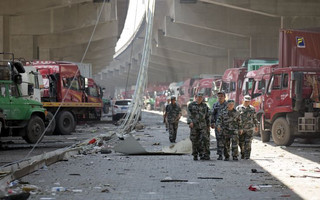 Security personnel walk between damaged trucks near the explosion site takes pictures of pluming smoke in Binhai new district in Tianjin, China August 13, 2015. Two huge explosions tore through an industrial area where toxic chemicals and gas were stored in the northeast Chinese port city of Tianjin, killing at least 44 people, including at least a dozen fire fighters, officials and state media said on Thursday. REUTERS/Damir Sagolj
