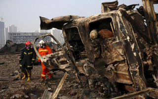 Firefighters walk past a damaged truck at the site of Wednesday night's explosions in Binhai new district of Tianjin
