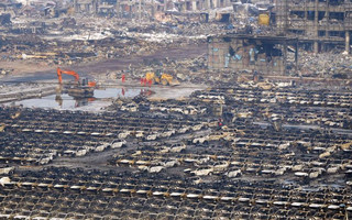 Rescuers walk next to damaged vehicles at the site of Wednesday night's explosions in Binhai new district of Tianjin
