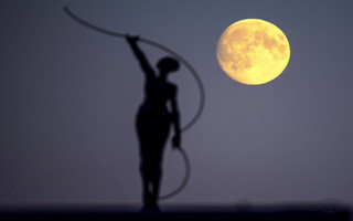 A statue is seen silhouetted against the moon in Brussels, Belgium