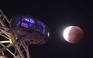 A supermoon is seen during a lunar eclipse behind pods of the London Eye wheel in London