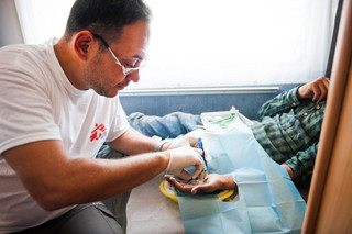MSF doctor Dimitri Giannousis inside a mobile clinic at the port of Mytiline, treats an Afghan teenager who burned his left hand in a forest fire in Turkey.