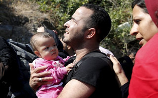 An Afghan migrant carrying a baby looks at a slope to climb, moments after arriving on a dinghy on the island of Lesbos