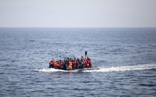 Syrian refugees on a dinghy wave as they approach the Greek island of Lesbos