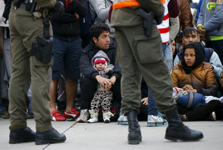 Members of the Austrian army guard a group of migrants waiting for transport at the Austrian border in Spielfeld, Austria, October 20, 2015. Slovenia will ask the European Union to send additional police forces to its border with Croatia to help it deal with thousands of migrants streaming into the tiny country on their way to Austria and beyond. About 6,000 migrants had entered Austria from Slovenia on Tuesday, a police spokesman in Styria province said. About 3,000 had arrived on Monday. REUTERS/Leonhard Foeger