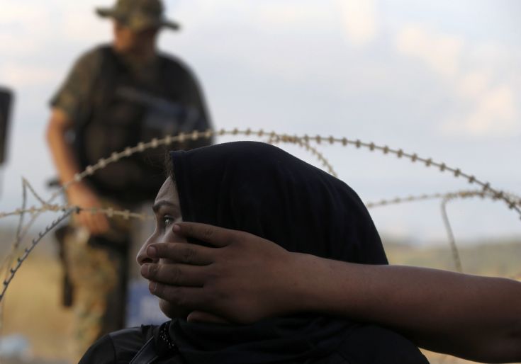 A Macedonian riot policeman stands guard as a Syrian refugee woman sits behind barbed-wire at the Greek-Macedonian border, near the village of Idomeni, August 21, 2015. Macedonian police fired tear gas and stun grenades to drive migrants and refugees back from its southern border from Greece on Friday but crowds continued to build up at a new bottleneck in an increasingly desperate flight to western Europe. At least 10 people were hurt in the brief flare-up, a day after the impoverished Balkan country declared a state of emergency on its border to halt a daily influx of up to 2,000 Syrians, Afghans, Iraqis and others heading north.   REUTERS/Yannis Behrakis