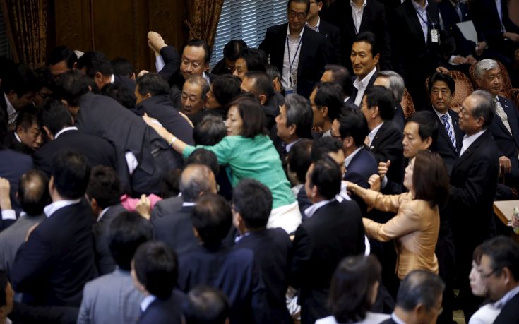 Japan's PM Abe sits next to Defense Minister Nakatani as he looks at lawmakers crowding around Konoike, chairman of the upper house special committee on security, during a vote at the parliament in Tokyo