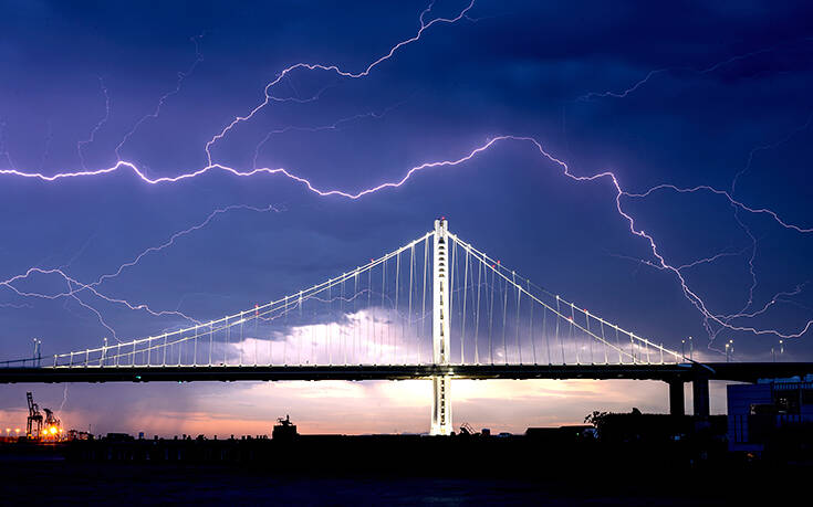 Молния разветвляется над мостом через залив Окленд в Сан-Франциско, когда над Оклендом, Калифорния, проходит шторм. Воскресенье, авг. 16 2020 Associated Press, лучшие фотографии недели