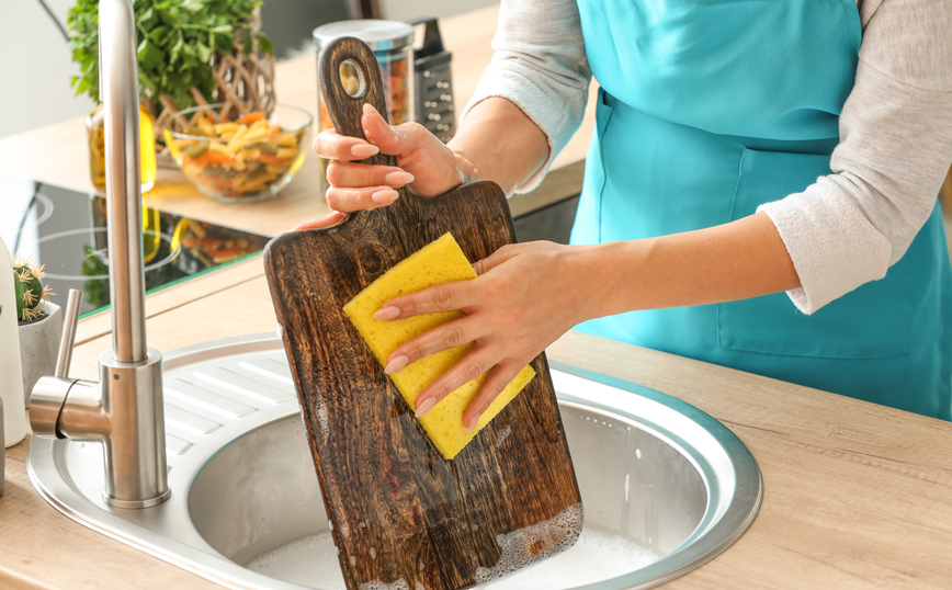 Γυναίκα πλένει το ξύλο κοπής στην κουζίνα Γυναίκα πλένει το ξύλο κοπής στην κουζίνα