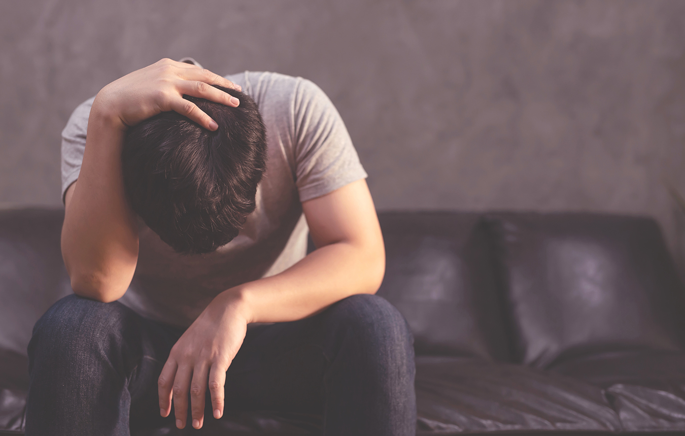 Άντρας κάθεται σε καναπέ με σκυμμένο το κεφάλι Άντρας κάθεται σε καναπέ με σκυμμένο το κεφάλι