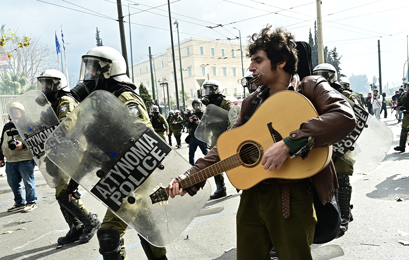 Διαδηλωτής παίζει κιθάρα δίπλα στα ΜΑΤ τη στιγμή των επεισοδίων στο Σύνταγμα – Δείτε φωτογραφίες