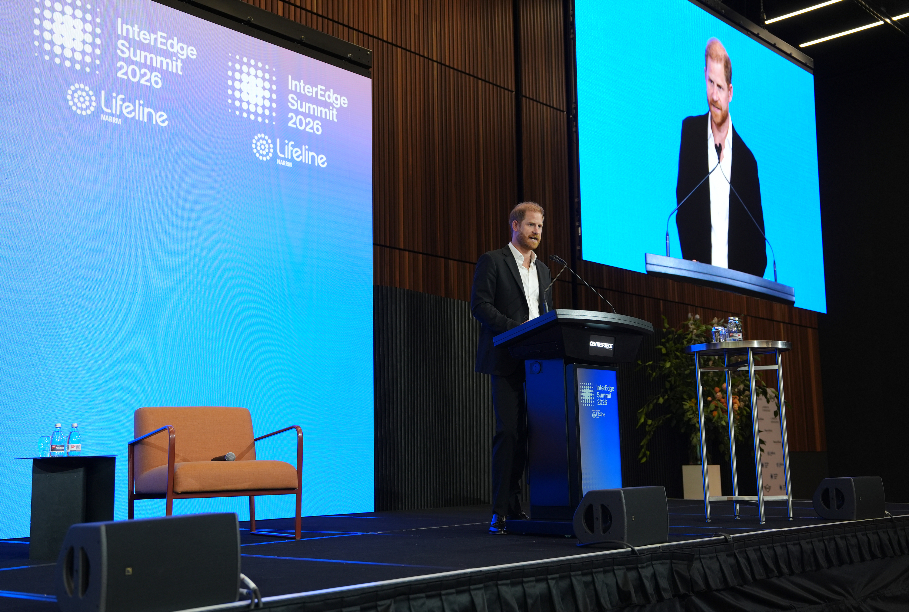 Ο πρίγκιπας Χάρι στέκεται πίσω από ένα βήμα ομιλητή, φορώντας σκούρο κοστούμι, και μιλάει σε εκδήλωση στην Αυστραλία