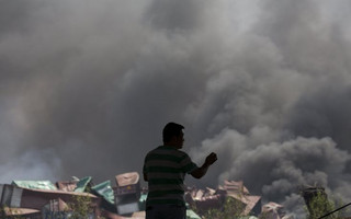A man looks at smoke pluming from the explosion site in Binhai new district in Tianjin, China August 13, 2015. Two huge explosions tore through an industrial area where toxic chemicals and gas were stored in the northeast Chinese port city of Tianjin, killing at least 44 people, including at least a dozen fire fighters, officials and state media said on Thursday. REUTERS/Damir Sagolj