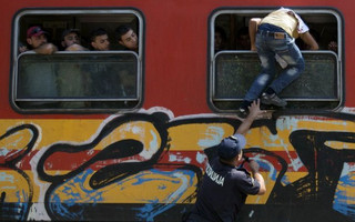 A policeman tries to stop a migrant from boarding a train through the window at Gevgelija train station in Macedonia, close to the border with Greece, August 15, 2015. In the past month, an estimated 30,000 refugees have passed through Macedonia, another step in their uncertain search for a better life in western Europe.  REUTERS/Stoyan Nenov