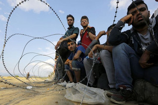 Syrian refugees sit in front of barbed-wire at the Greek-Macedonian border, near the village of Idomeni, August 21, 2015. Macedonian police fired tear gas and stun grenades to drive migrants and refugees back from its southern border from Greece on Friday but crowds continued to build up at a new bottleneck in an increasingly desperate flight to western Europe. At least 10 people were hurt in the brief flare-up, a day after the impoverished Balkan country declared a state of emergency on its border to halt a daily influx of up to 2,000 Syrians, Afghans, Iraqis and others heading north.   REUTERS/Yannis Behrakis