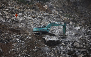 A rescue worker is seen next to a excavator as a search is conducted at the site of a mining factory after a landslide hit Shanyang county