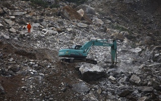 A rescue worker is seen next to a excavator as a search is conducted at the site of a mining factory after a landslide hit Shanyang county