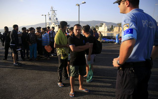 A migrant waits in line next to a Frontex officer at the port of Kos, following a rescue operation off the Greek island of Kos
