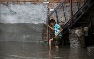 A boy holds onto a stair railing as he walks in floodwaters flowing from the swollen Bagmati River brought on by heavy rainfall in Kathmandu