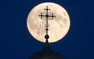 A cross atop of a local monastery is seen silhouetted against the moon in the settlement of Poschupovo in Ryazan region