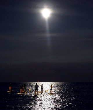 Stand up paddle boarders paddle under the supermoon off the beach in Barcelona