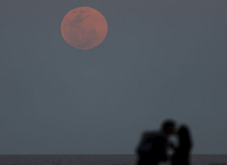 A couple kisses as a supermoon rises in the sky over the Rio de La Plata in Buenos Aires