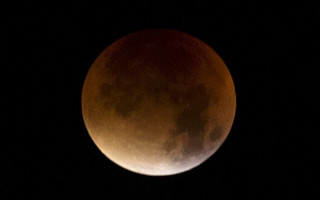 The Moon, appearing a dim red colour, is covered by the Earth's shadow during a total lunar eclipse over Dover in southern England