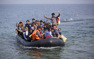 Syrian and Afghan refugees on a dinghy wave as they approach the Greek island of Lesbos September 3, 2015. The International Organization for Migration (IOM) says 1,500-2,000 are taking the route through Greece, Macedonia and Serbia to Hungary every day and that there is "a real possibility" the flow could rise to 3,000 daily. REUTERS/Dimitris Michalakis