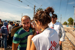 MSF Doctor, Stavroula Kostaki, checks the temperature of a patient in a queue.  He is feeling ill but he does not want to leave his group because he is about to cross the border to Macedonia at Idomeni.