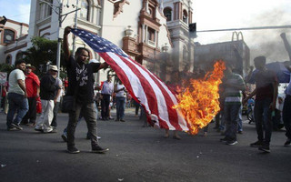An opposition supporter burns a flag of the United States, who recognized disputed election results handing victory in November's presidential election to incumbent Juan Orlando Hernandez, during a march and rally led by opposition leader Salvador Nasralla in San Pedro Sula, Honduras, Saturday, Jan. 6, 2018. Following an election marred by irregularities, Hernandez was declared the victor and will be inaugurated on Jan. 27. Nasralla reaffirmed his claim on the presidency and said he would not stop calling for protests and civil disobedience until Hernandez agrees to step down. (AP Photo/Fernando Antonio)