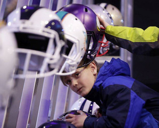 Beau Befort, 8, tries to slip his head into one of the helmets on display at the NFL Experience football fan attraction Friday, Feb. 2, 2018, in Minneapolis. The New England Patriots and the Philadelphia Eagles are scheduled to play in Super Bowl 52 Sunday, Feb. 4. (AP Photo/Mark Humphrey)
