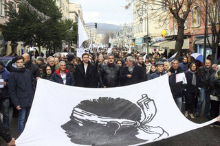 Residents of the Corsica island, take the streets behind a flag featuring a Moor's head, the Corsican emblem, in Ajaccio, France, as they demonstrate ahead of a visit to the Mediterranean island next week by French President Emmanuel Macron, Saturday, Feb. 3, 2018. Corsica's newly elected leaders want new talks with the government about their demands, including equal status for the Corsican language and the release of Corsican prisoners held in mainland prisons. (AP Photo/Raphael Poletti)