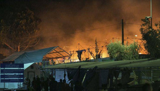 Riot police stand guard as a large fire burns inside the Moria refugee camp on the northeastern Greek island of Lesbos, late Monday, Sept. 19. 2016. Greek police say a large fire swept through the big camp for refugees and other migrants on the eastern Aegean island of Lesbos, forcing its evacuation. None of the more than 4,000 people in the Moria camp was reported injured in Monday's blaze, which damaged tents and prefabricated housing units. (AP Photo/Michael Schwarz)