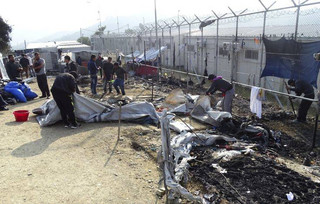 Refugees help clear the Moria refugee camp after a fire on the northeastern Greek island of Lesbos, on Friday, Nov. 25, 2016. Police say two people have died on the Greek island of Lesbos and two others were seriously injured after a fire raged through a refugee camp used for migrants facing deportation back to Turkey. (AP Photo)