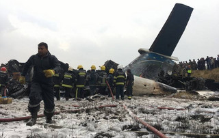 Nepalese rescuers stand near a passenger plane from Bangladesh that crashed at the airport in Kathmandu, Nepal, Monday, March 12, 2018. (AP Photo/Niranjan Shreshta)