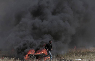A Palestinian protester burns tires during clashes with Israeli troops along Gaza's border with Israel, Friday, April 6, 2018. Palestinians torched piles of tires near Gaza's border with Israel on Friday, sending huge plumes of black smoke into the air and drawing Israeli fire that killed one man in the second large protest in the volatile area in a week. (AP Photo/Adel Hana)