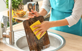 Γυναίκα πλένει το ξύλο κοπής στην κουζίνα