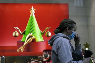 Γυναίκα φτιάχνει την μάσκα της μπροστά από χριστουγεννιάτικη βιτρίνα μαγαζιού