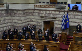 Greek Cabinet and lawmakers applaud as Ukrainian President Volodymyr Zelenskyy, on the screen, thanks after addressing Greek Parliament in Athens, Greece, Thursday, April 7, 2022. Zelenskyy called for more weapons to be sent from the West to Ukraine, and for tightened sanctions on Russia that would ban all Russian banks from doing business abroad, and bar Russian commercial ships from ports across the world