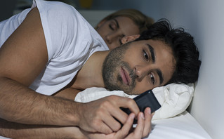 Άντρας ξύπνιος στο κρεβάτι κοιτάει το κινητό του
